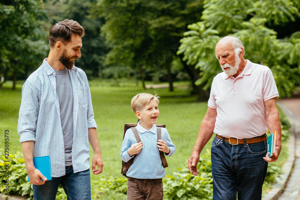 Three different generations together Affectionate dad and granddad seeing their little boy off to elementary school. Mans support, love, parentship, care concept. Back to school. First day of fall.