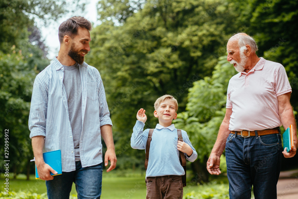 Dad and gfandfather seeing their son or grandson off to school. Three generation happy family walking, talking outdoor in nature park. Dad and gfandfather seeing their son or grandson off to school. Three generation happy family walking, talking outdoor in nature park.