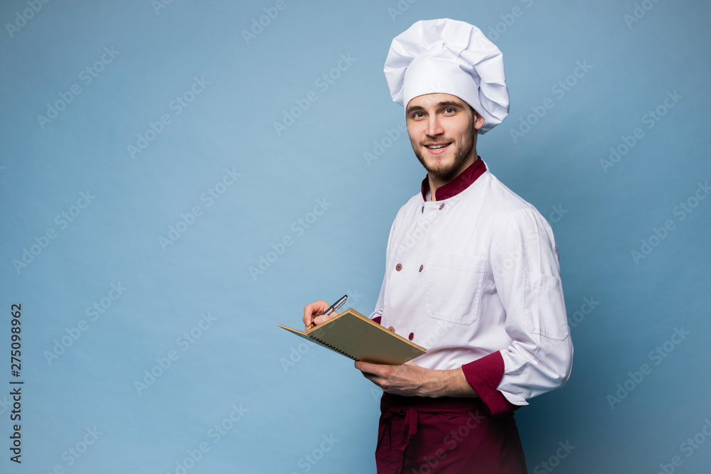 Portrait of a professional chef in uniform holding recipe book and looking at camera on light blue. Portrait of a professional chef in uniform holding recipe book and looking at camera on light blue.