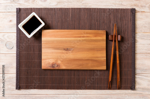 Empty rectangular wooden plate for sushi with sauce and chopsticks on wooden table, top view