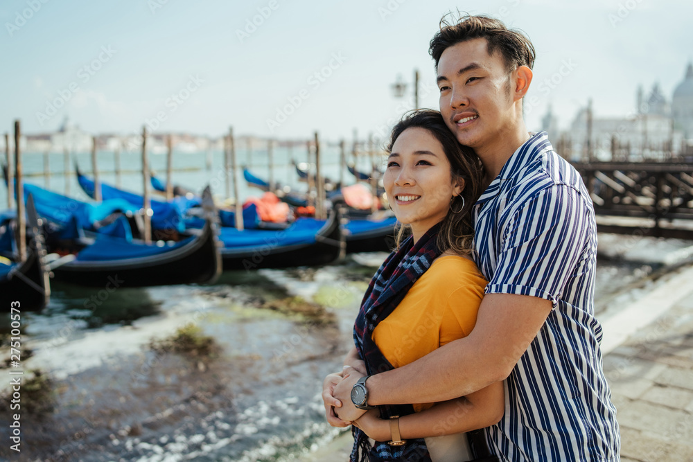 Loving couple on vacation in Venice, Italy - Millennials hugged on the quay, behind them the gondolas and the lagoon