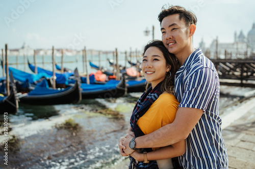 Loving couple on vacation in Venice, Italy - Millennials hugged on the quay, behind them the gondolas and the lagoon © loreanto