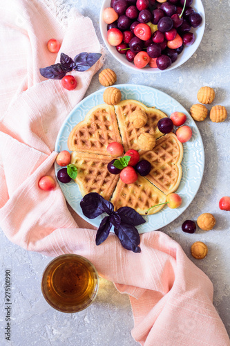 Belgian waffles on a plate with cherry and tea top view on a gray background