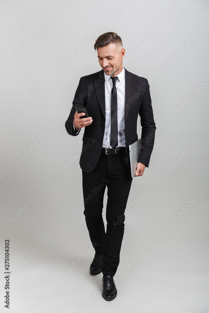 Photo of handsome adult businessman in formal suit smiling while holding laptop and cellphone Photo of handsome adult businessman in formal suit smiling while holding laptop and cellphone