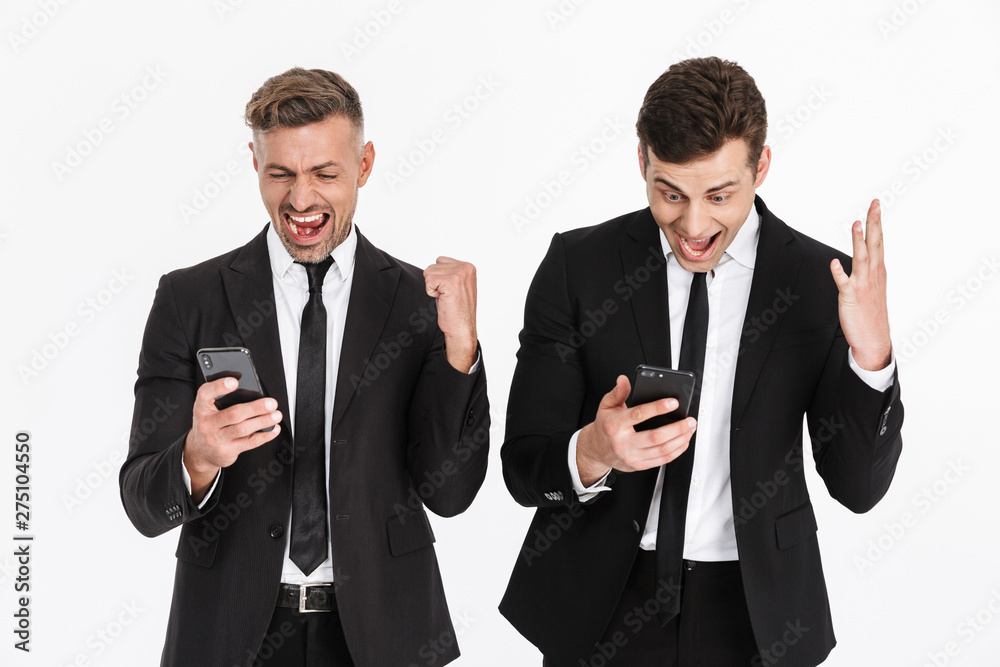 Image of delighted caucasian two businessmen in office suits rejoicing and screaming while holding cellphones Image of delighted caucasian two businessmen in office suits rejoicing and screaming while holding cellphones