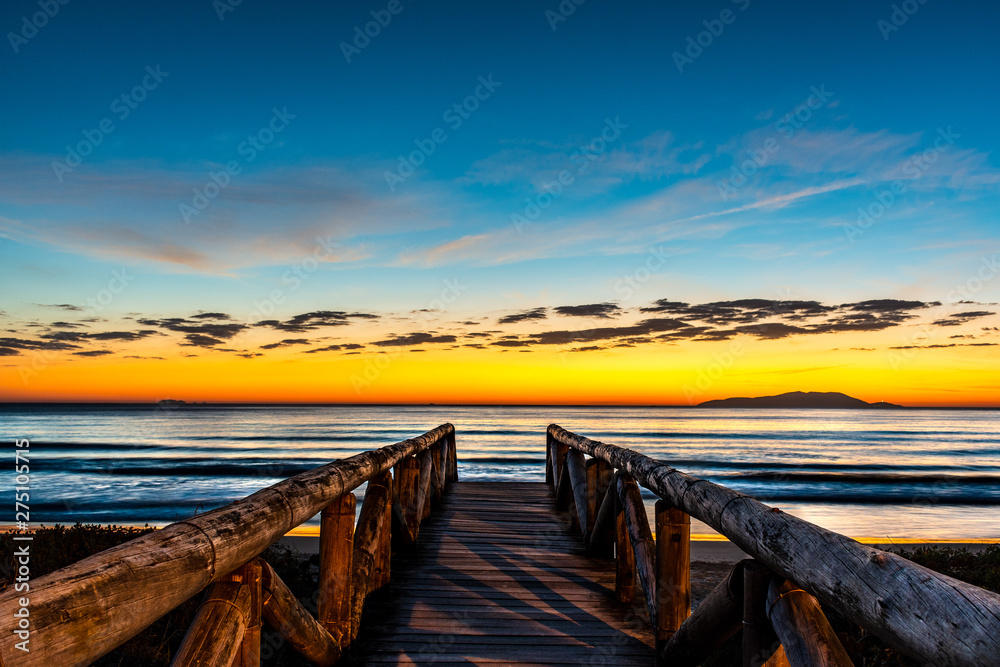 beautiful landscape with wooden walkway to seascape beach at sunrise with blue and orange sky and island in the background