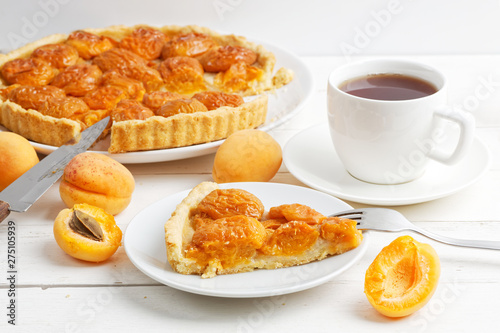 Homemade apricot pie with fresh fruits and cup of tea on white wooden table. Shallow focus.