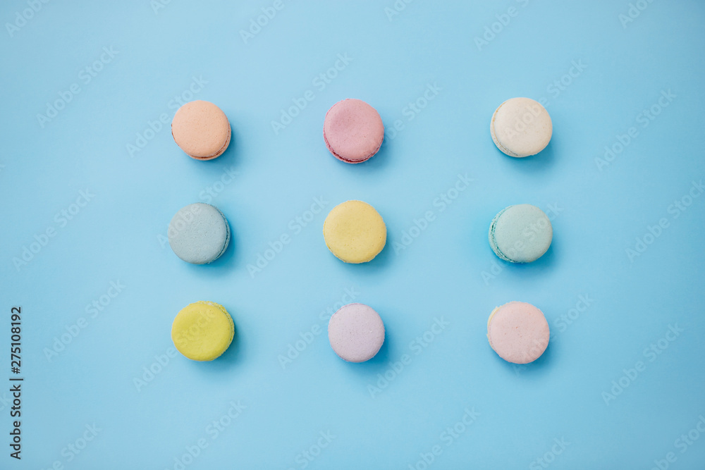 Top view of sweet colorful French macaroon biscuits lying in three lines on pastel blue backgroud. Top view of sweet colorful French macaroon biscuits lying in three lines on pastel blue backgroud.