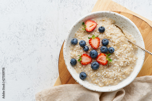 Oatmeal porridge rustic with berries, dash diet, on white wooden background top view