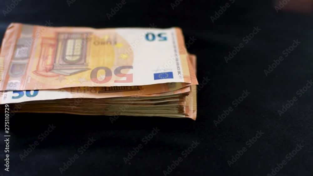 A sliding, right to left shot of a female's hand taking fifty euro bills from a money stack. Around two thousand euros in the stack, sitting on a black table-top cloth. A sliding, right to left shot of a female's hand taking fifty euro bills from a money stack. Around two thousand euros in the stack, sitting on a black table-top cloth.