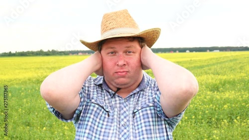 I need silence. Young man covering ears with hands while standing against against field on a sunny day photo