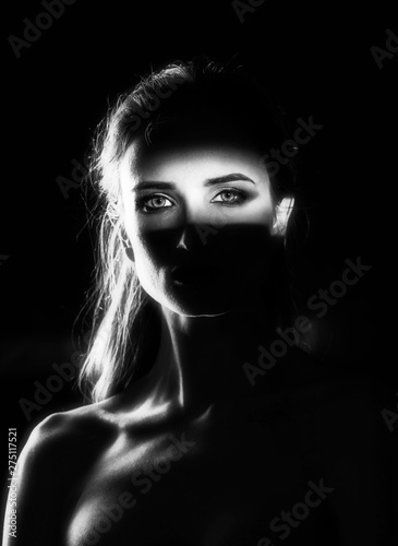 Beautiful girl model with red lips make up and naked shoulders in the shade, with a lit silhouette and a strip of light illuminating her eyes. Conceptual, art, fashionable design. Black and white