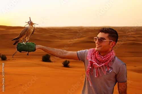 portrait of a young man with a falcon on his hand in a desert at sunset