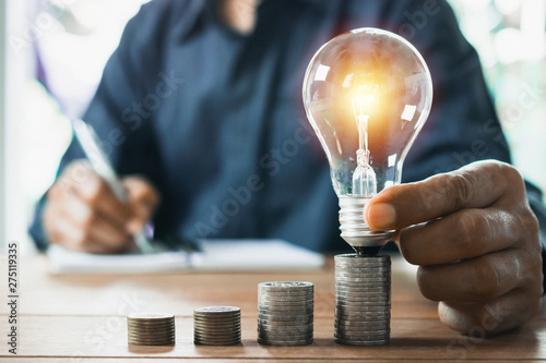 Business man holding light bulb on the desk in office and writing on note book it for financial,accounting,energy,idea concept.