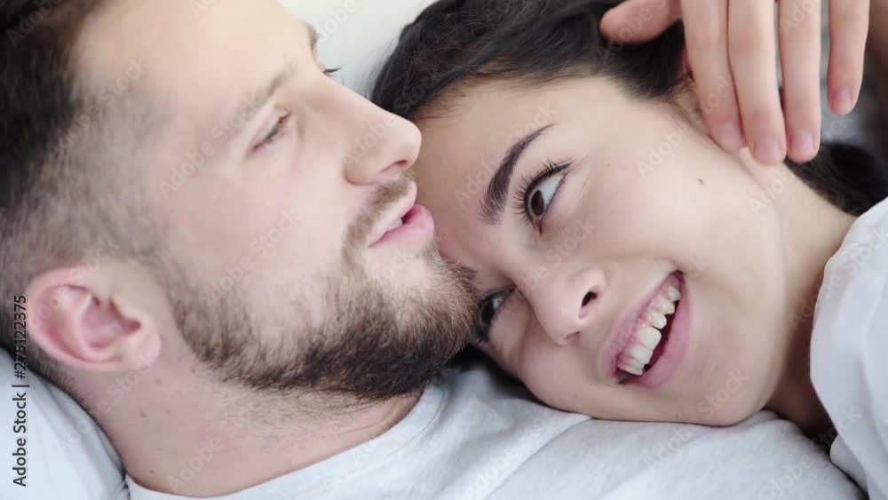 close up of happy man touching face and hair of cheerful woman while kissing and lying on bed close up of happy man touching face and hair of cheerful woman while kissing and lying on bed