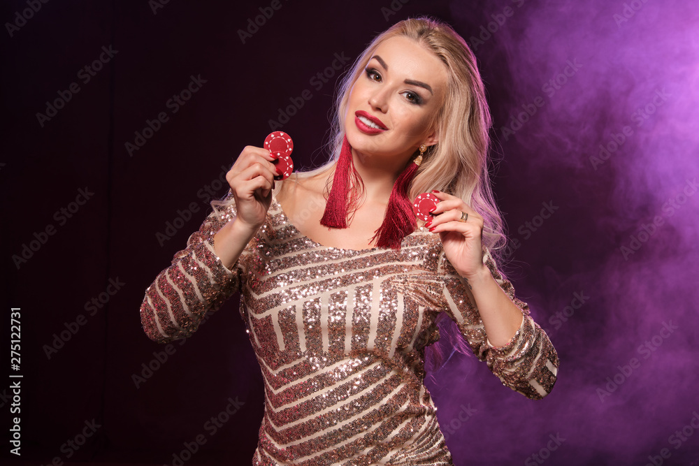 Blonde woman with a perfect hairstyle and bright make-up is posing with gambling chips in her hands. Casino, poker.