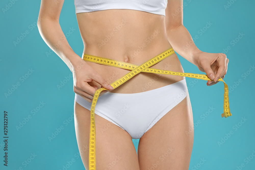 Slim young woman with smooth gentle skin in underwear measuring body on color background, closeup