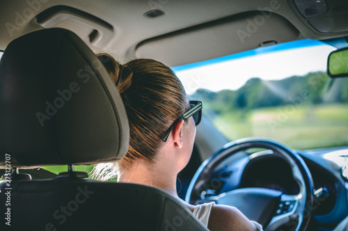 Young woman with brown hair wearing sunglasses driving car while looking forward – Girl sitting inside of a modern vehicle in the driver’s seat