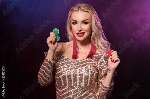 Blonde woman with a perfect hairstyle and bright make-up is posing with gambling chips in her hands. Casino, poker.