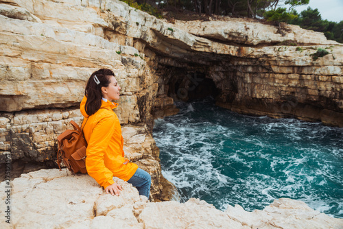 young woman sitting at cliff looking at grotto cave with blue azure water © phpetrunina14
