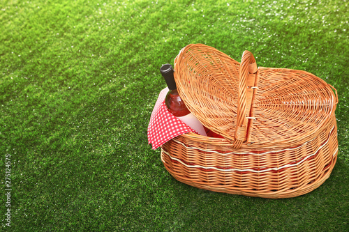 Picnic basket with bottle of wine on grass, space for text