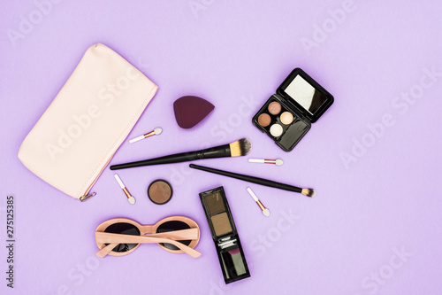 Makeup brushes; eyeshadow palette and sunglasses on purple backdrop