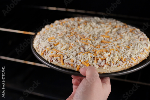 Person placing a frozen cheese pizza into a hot oven for baking in a home kitchen