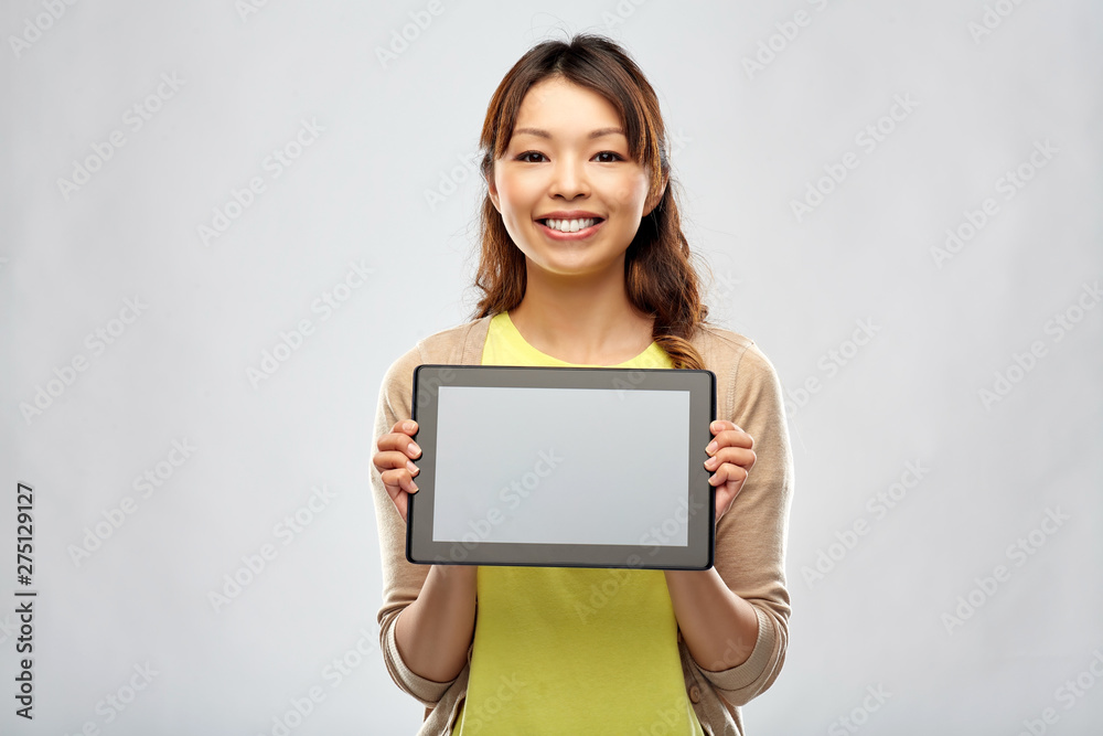 technology and people concept - happy asian woman showing tablet computer over grey background technology and people concept - happy asian woman showing tablet computer over grey background