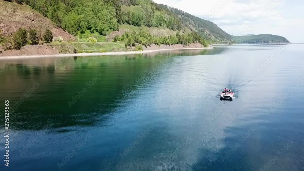 Aerial, top drone scene of catamaran anchored in a bay with transparent turquoise water and patterned bottom. Camera slowly moves to the sides to the coast. Lake Baikal. Aerial, top drone scene of catamaran anchored in a bay with transparent turquoise water and patterned bottom. Camera slowly moves to the sides to the coast. Lake Baikal.