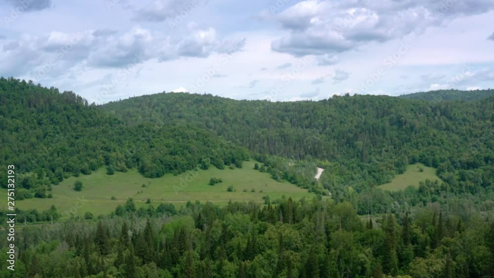 The unpaved white uphill road.The road follows between mountaind into the forest. Aerial follow shot.The camera crossing the river, trees and green hill. The unpaved white uphill road.The road follows between mountaind into the forest. Aerial follow shot.The camera crossing the river, trees and green hill.