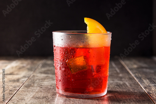 Negroni cocktail with piece of orange in glass on wooden table