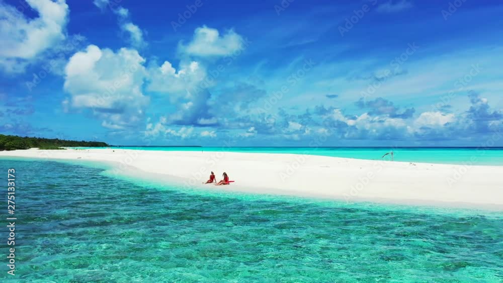Aerial view of three young women in red bathing cloths sitting on a white sandy beach. the turquoise water of the Bahamas, a dramatic sky above. Truck left, dolly in Aerial view of three young women in red bathing cloths sitting on a white sandy beach. the turquoise water of the Bahamas, a dramatic sky above. Truck left, dolly in