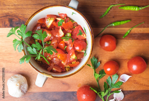 Top view of tomato salad with basil  olive oil  garlic  chilli and balsamic vinegar in bowl over wooden background