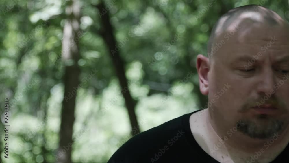 A man stands in forest looking up at sky in slow motion. He looks serious, sombre and contemplative. Dark shadows of trees and sunlight. A man stands in forest looking up at sky in slow motion. He looks serious, sombre and contemplative. Dark shadows of trees and sunlight.