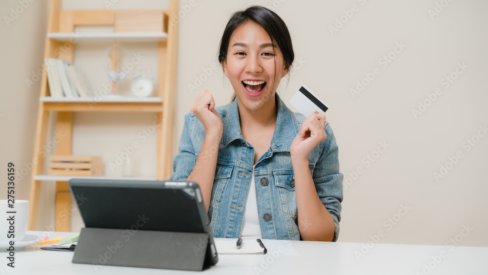 Beautiful smart business Asian woman using tablet buying online shopping by credit card while wear smart casual sitting on desk in living room at home. Lifestyle woman working at home concept. Beautiful smart business Asian woman using tablet buying online shopping by credit card while wear smart casual sitting on desk in living room at home. Lifestyle woman working at home concept.