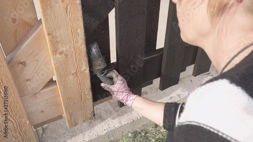 women painting a large carport with black wood paint Slowmotion 100fps photo