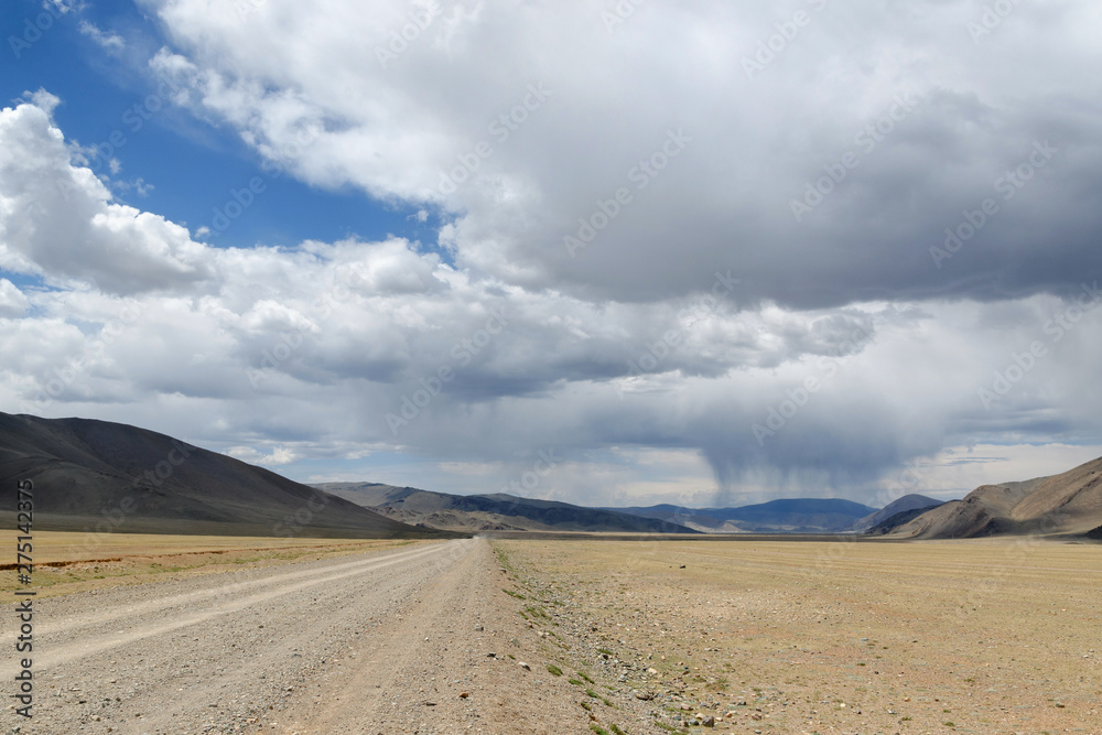 Western Mongolia steppe landscape. Dirt road and rain ahead. Outskirts Tsagaannuur, Bayan-Ulgii Province, Mongolia.
