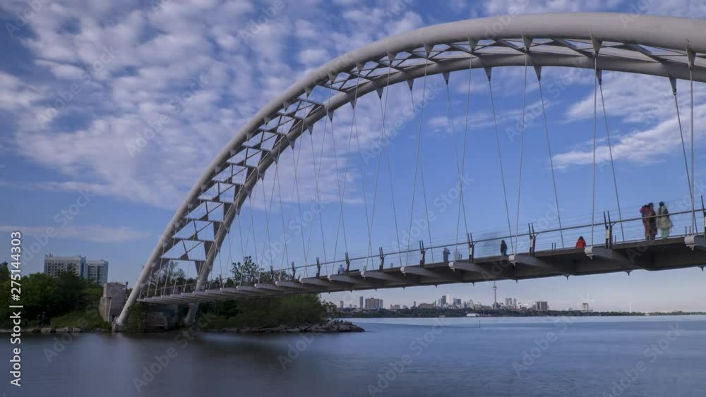 Timelapse of Humber Bay Arch Bridge shot with long exposure as people walk on the bridge and white clouds move on blue sky. 4K ProRes 444. Toronto waterfront, Canada. Summer time, sunny day. Timelapse of Humber Bay Arch Bridge shot with long exposure as people walk on the bridge and white clouds move on blue sky. 4K ProRes 444. Toronto waterfront, Canada. Summer time, sunny day.