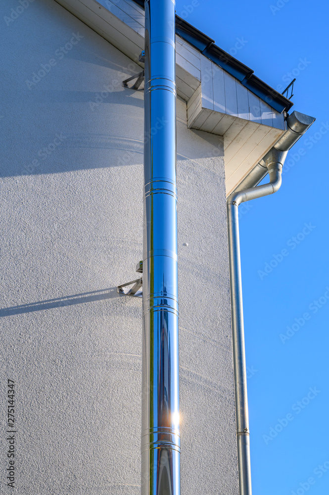 Stainless steel chimney and parts of a roof in front of a bright blue sky. Stainless steel chimney and parts of a roof in front of a bright blue sky.