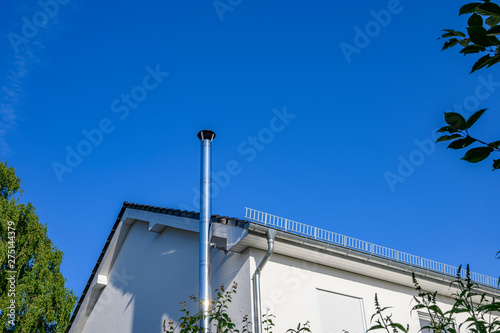 Stainless steel chimney and parts of a roof in front of a bright blue sky.