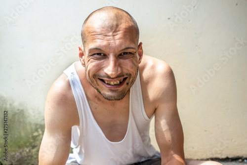 Canvastavla Young skinny anorexic bald positive and happy smiling homeless man sitting on th