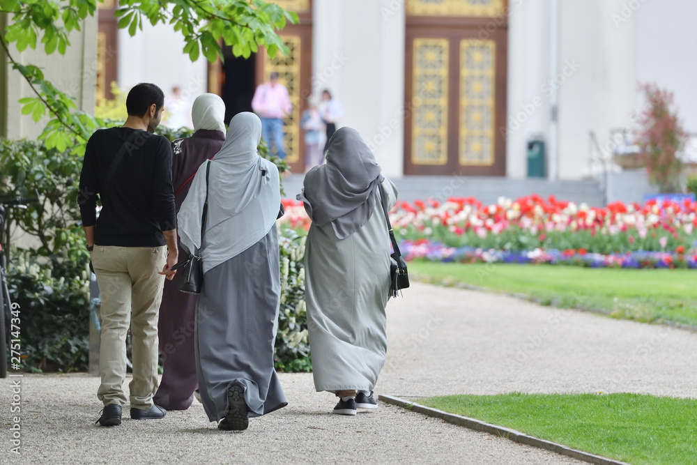A group of refugees from the Middle East, three women in hijabs and a man walk in the European park and go to the building. Germany, Baden Baden