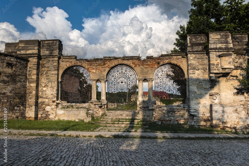 Forged iron gates against the sky with beautiful white clouds. The ruins of St. Nicholas Armenian Church XV century, Kamianets-Podilskyi, Ukraine.