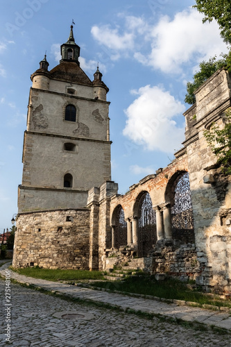 Bell tower, part of the wall and a forged iron gate on the background of the blue sky. Ruins of the Armenian Church of St. Nicholas of the XV century, Kamianets-Podilskyi, Ukraine.