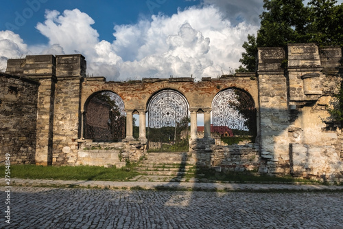 Forged iron gates against the sky with beautiful white clouds. The ruins of St. Nicholas Armenian Church XV century, Kamianets-Podilskyi, Ukraine.