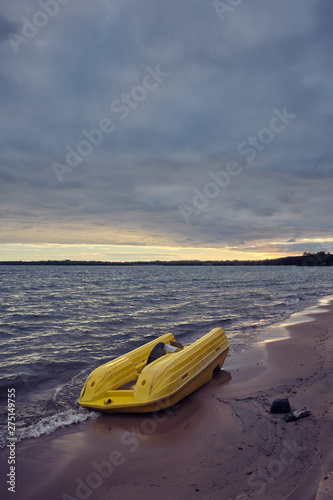 yellow pedal boat floating ashore and lying up and down the beach, dark clouds on the sky and beach in the foreground