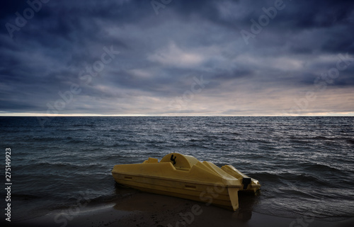 yellow pedal boat floating ashore on the beach, dark clouds in the sky and beach in the foreground and sunset in the background