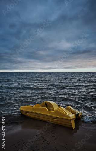 yellow pedal boat floating ashore on the beach, dark clouds in the sky and beach in the foreground and sunset in the background