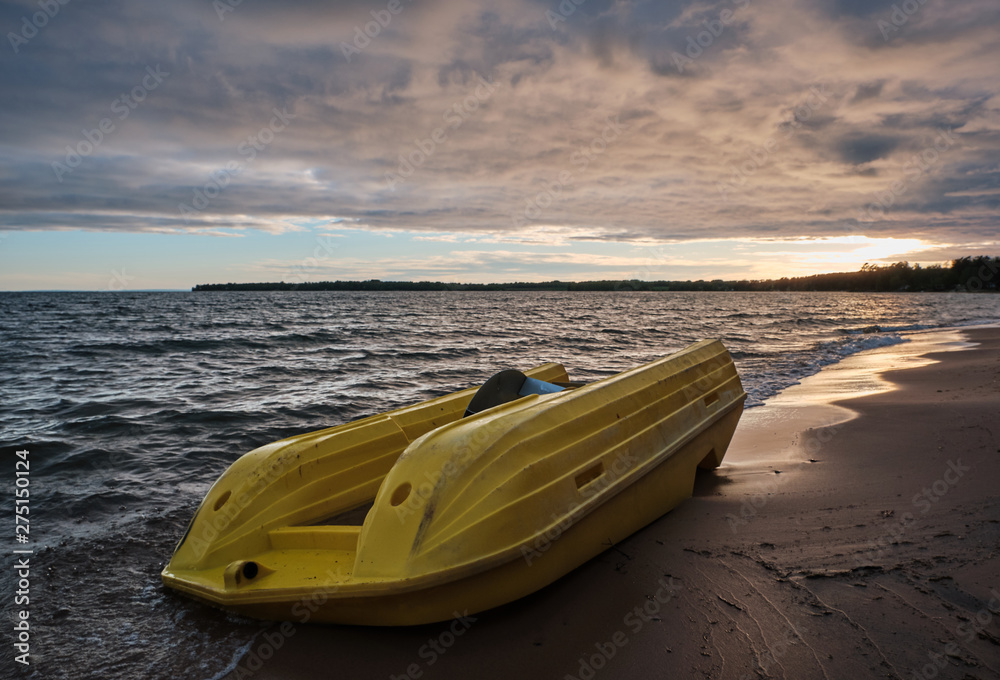 yellow pedal boat floating ashore and lying upside down on the beach, dark clouds in the sky and beach in the foreground and sunset in the background yellow pedal boat floating ashore and lying upside down on the beach, dark clouds in the sky and beach in the foreground and sunset in the background