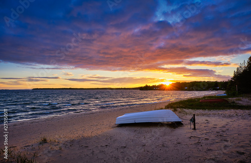 a small white boat lies up and down the beach, beautiful sunset in the background